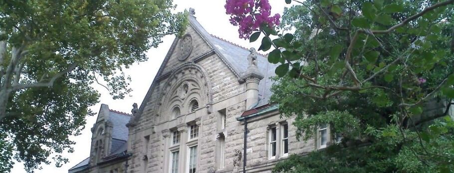 Classic stone college building with trees and flowers.