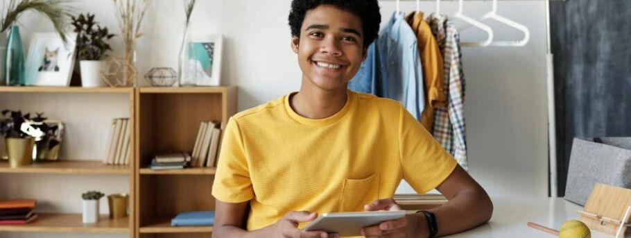 Smiling student using a tablet in a study space at home.