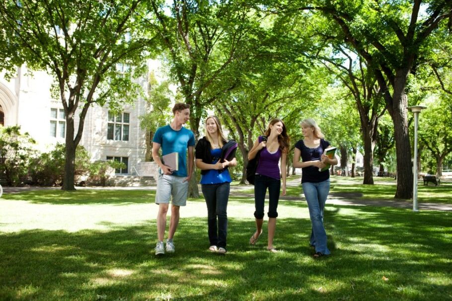 College students walk across a sunny, green campus lawn.