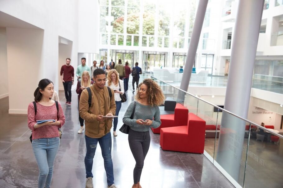 Diverse students walk in a modern university building, representing higher education.