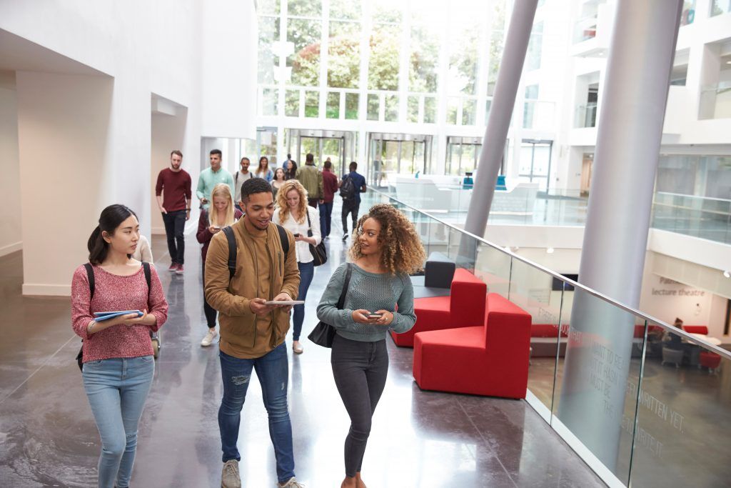 Diverse students walk in a modern university building, representing higher education.