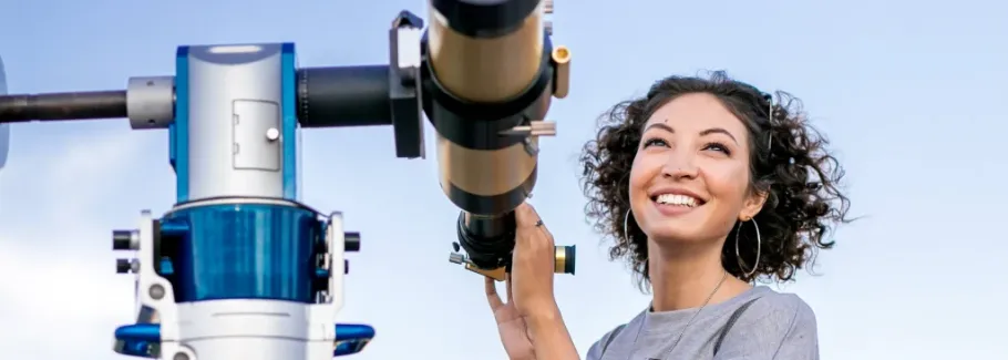 Smiling student looks through telescope, representing exploration and academic curiosity.