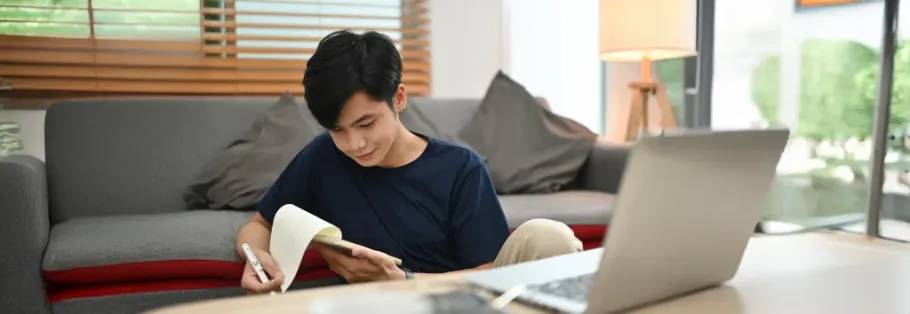 Student studying at home with laptop and notebook for college applications.