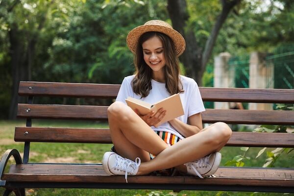 teenage girl reading on a park bench