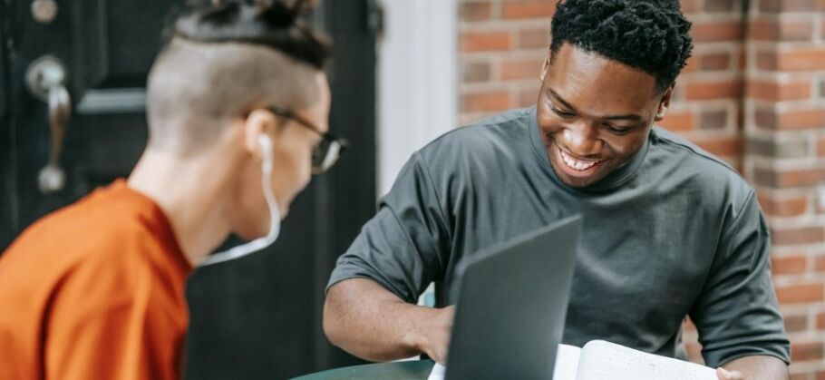 Two students collaborate on academics with a laptop and notebook.