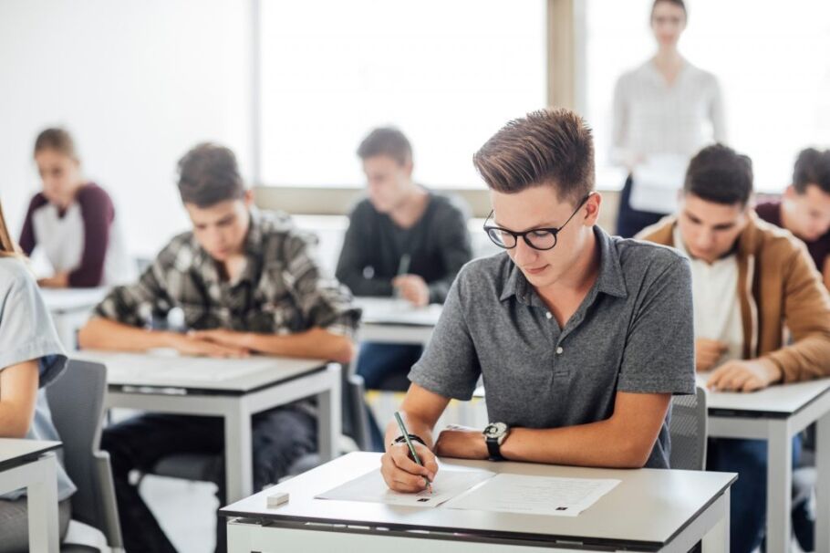 Students taking a test in a classroom setting with a teacher.