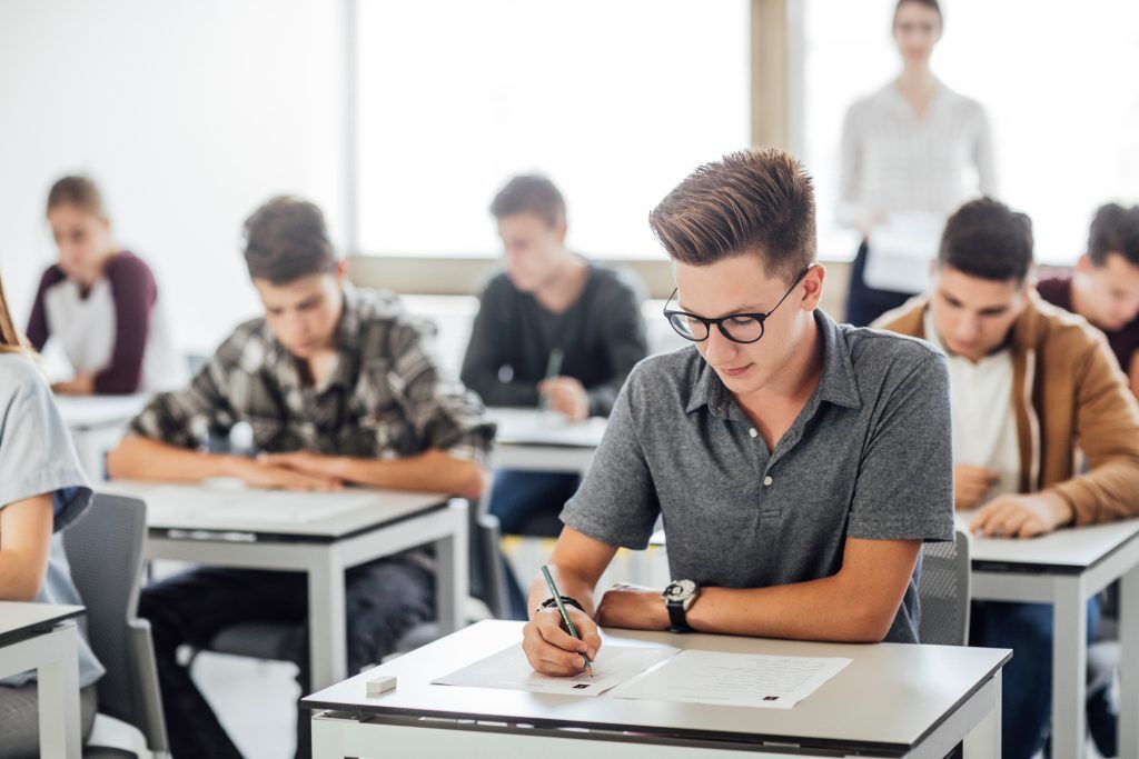 Students taking a test in a classroom setting with a teacher.