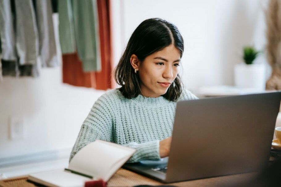 Student researches college options on laptop with notebook nearby.