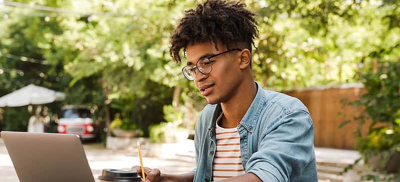 Student with laptop studies outdoors, preparing for college applications.