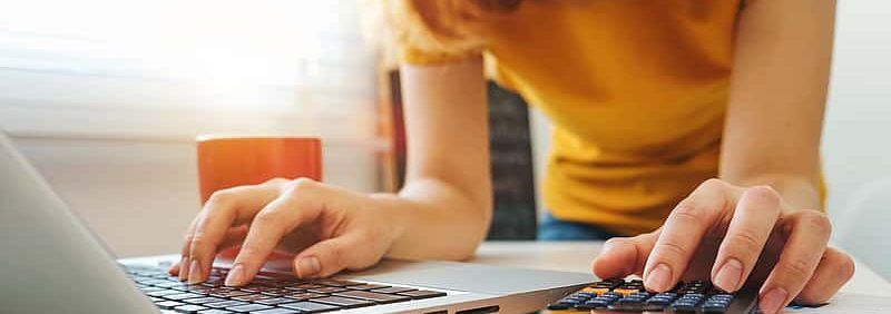 Student using a calculator and laptop for college financial planning.