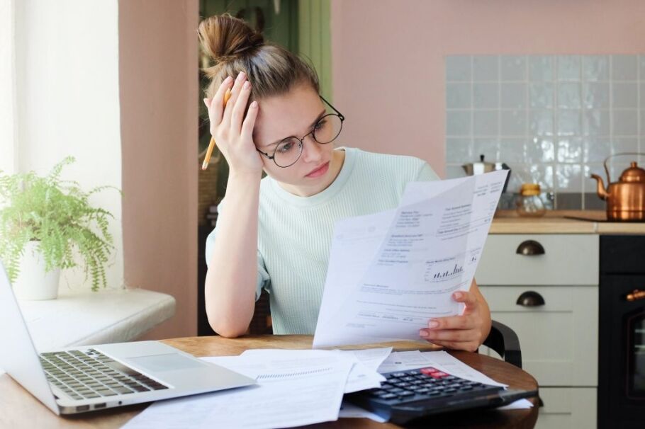Stressed student reviews college financial aid documents with laptop and calculator.