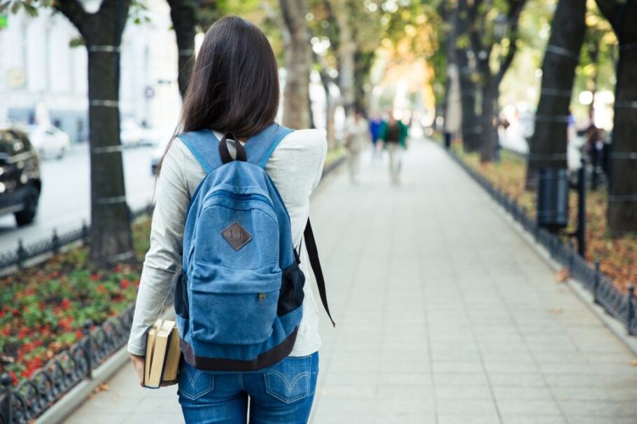 Student walks on campus with books and backpack, focused on the future.