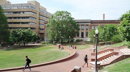 College campus scene with students walking on brick paths and green lawns.
