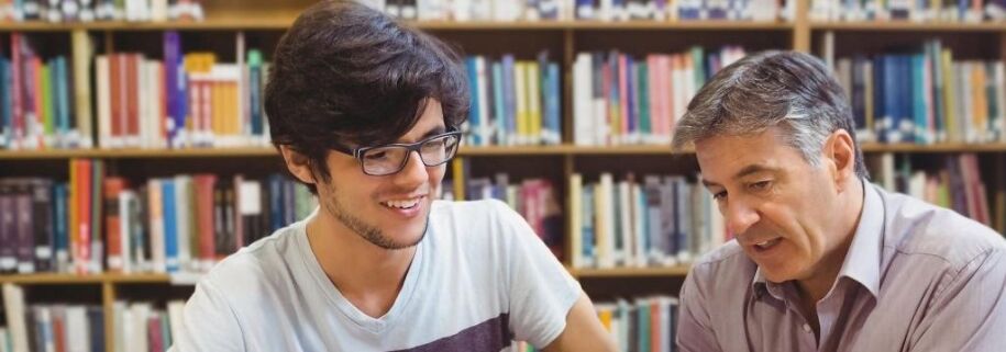 Student and counselor review college application essays in front of a bookshelf.
