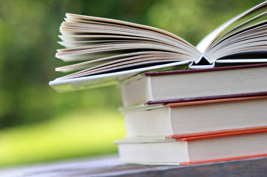 Stack of books with open book on top, green background.