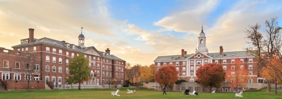 College campus buildings with autumn foliage and students relaxing on the lawn.