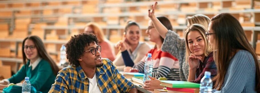 College students in a lecture hall, one raising their hand.