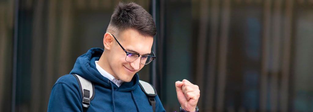 Student in glasses with backpack pumps fist in apparent academic success.
