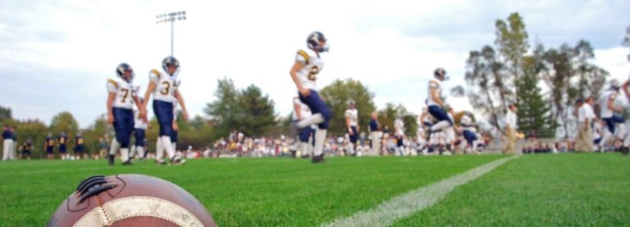 Football on the field with players practicing; athletics and college preparation.