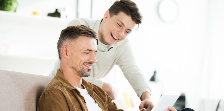 Father and son happily review college application options on a tablet.