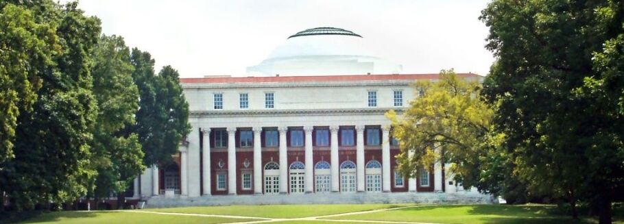 Classic college building with columns and dome, surrounded by green trees.