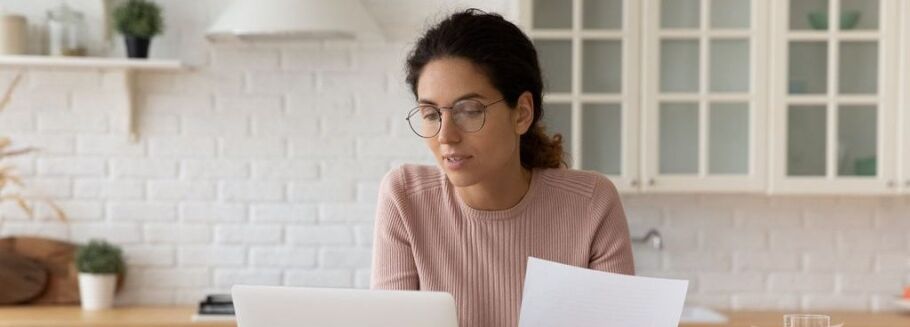 Student reviews college application essay on laptop with paper in hand.