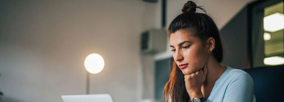 Student thoughtfully reviews college application essays on laptop.