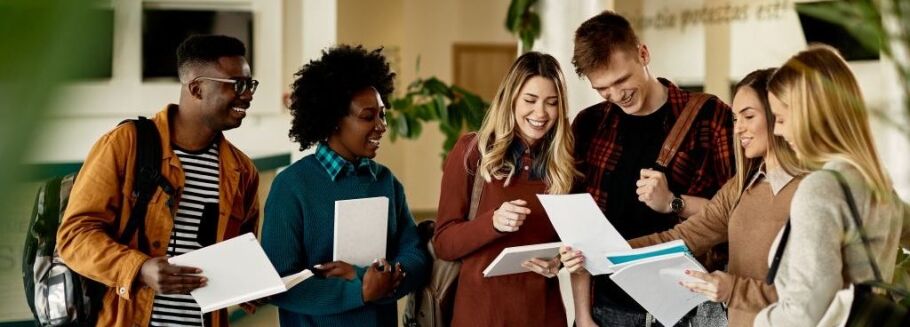 Smiling college students review documents together in a campus hallway.