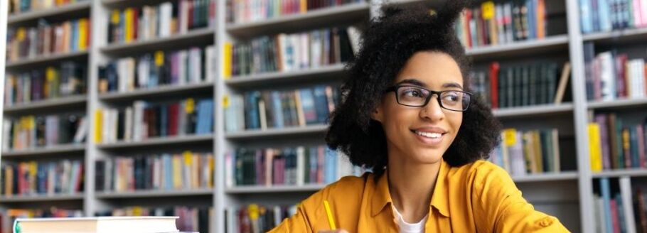 Smiling student studies in library, thinking about college and future success.
