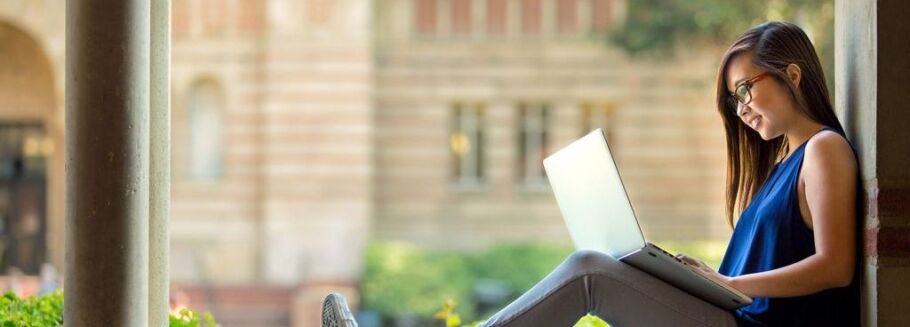 Student works on laptop in a campus courtyard, focused on academic success.