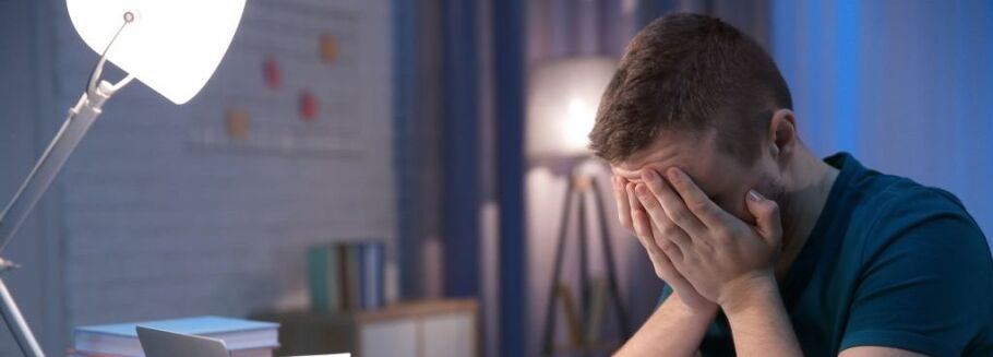 Stressed student with head in hands at desk, laptop, and books.