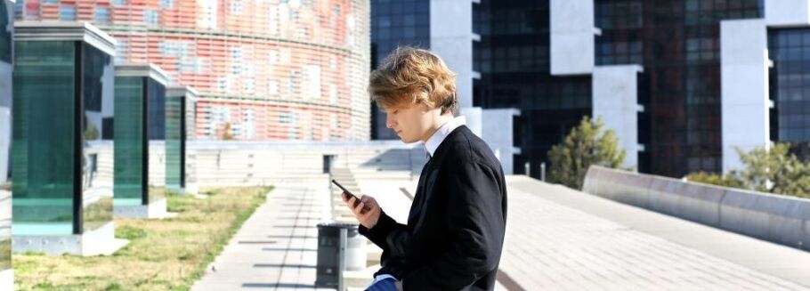Student checks college application status on phone in modern urban setting.