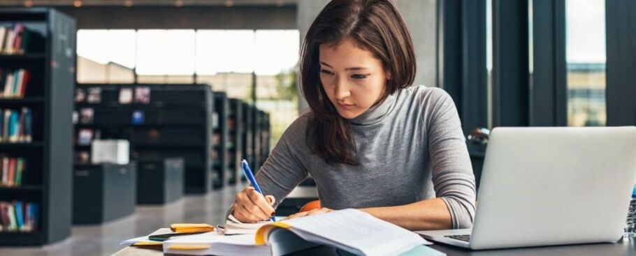 Student studying with laptop and books in library for college success.