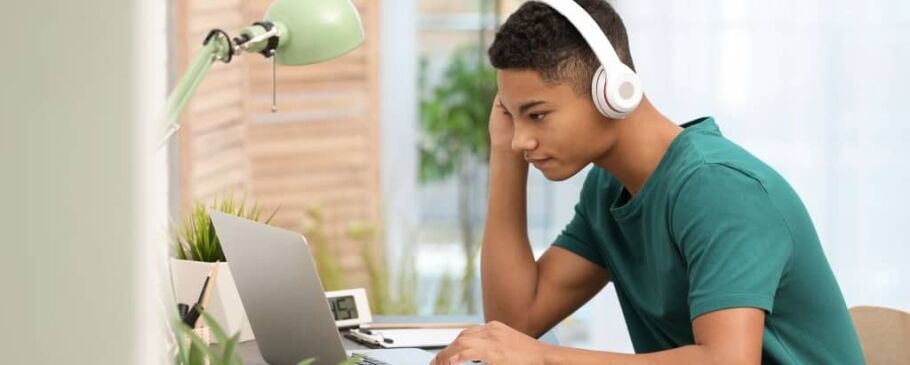 Teen student with headphones studies at a laptop for college prep.