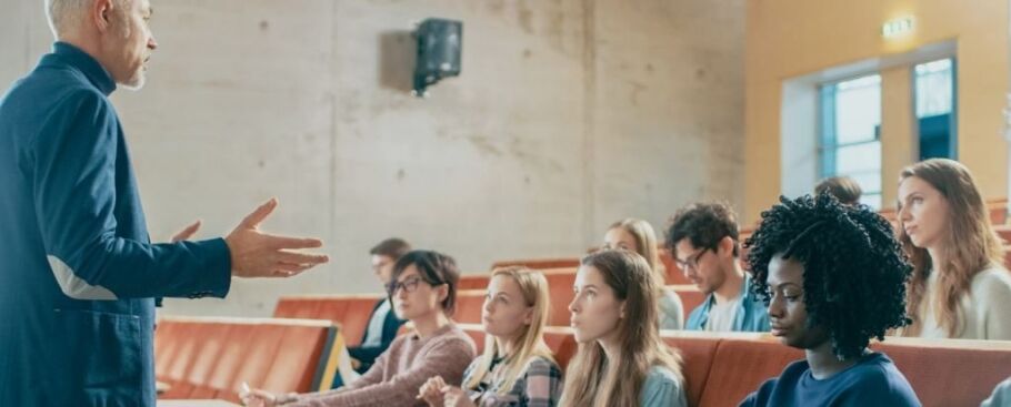 Professor lectures to diverse students in a college lecture hall.