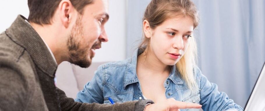 Counselor helps student with college application on laptop.