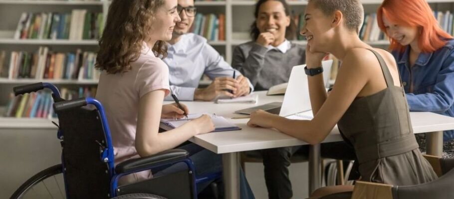 Diverse students collaborate at a table with books and a laptop.