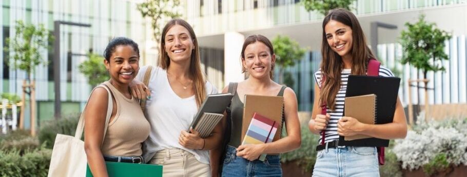 Smiling students with books on a college campus, ready for academic success.