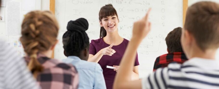 Teacher smiles while teaching chemistry to students in a classroom.