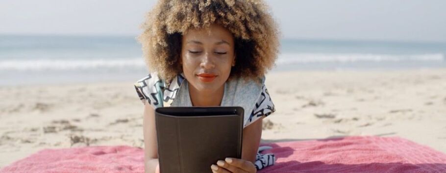 Student studies college application essays on tablet at the beach.