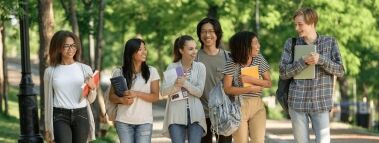 Diverse group of smiling students walking on a college campus path.
