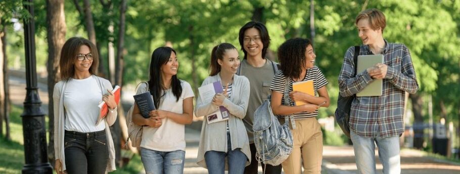 Diverse group of smiling students walking on a college campus path.