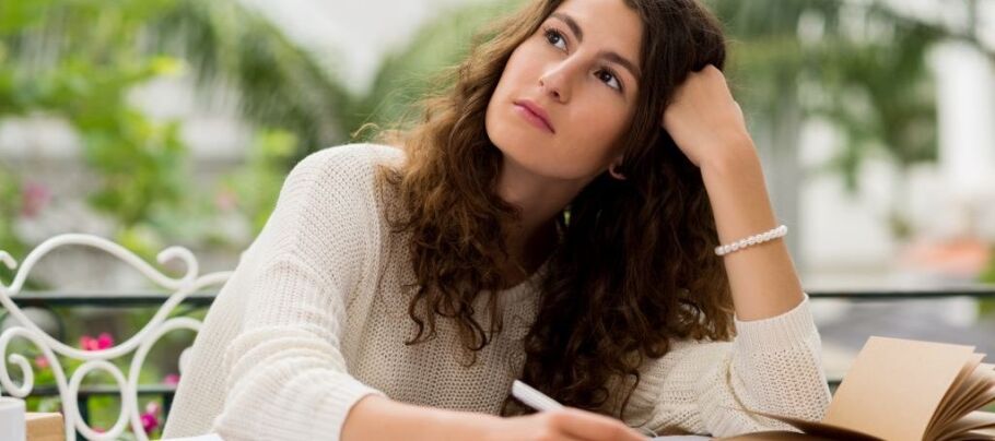 Student thoughtfully considers college essay ideas with pen and notebook.