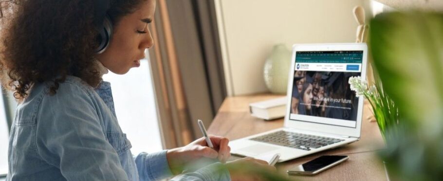 Student wearing headphones studies with IvyWise website on laptop.
