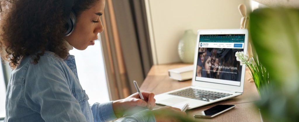 Student wearing headphones studies with IvyWise website on laptop.