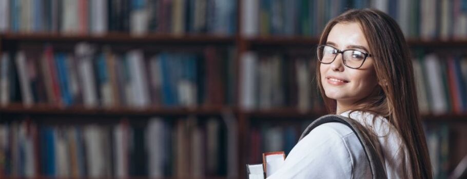 Smiling student with books in library, representing academic success and college preparation.