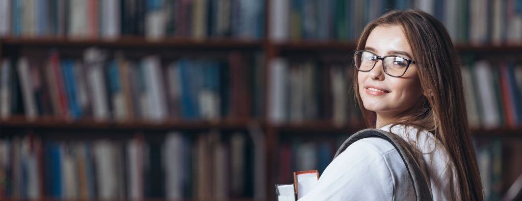 Smiling student with books in library, representing academic success and college preparation.