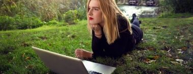 Student with laptop lying on grass, contemplating college application essays.