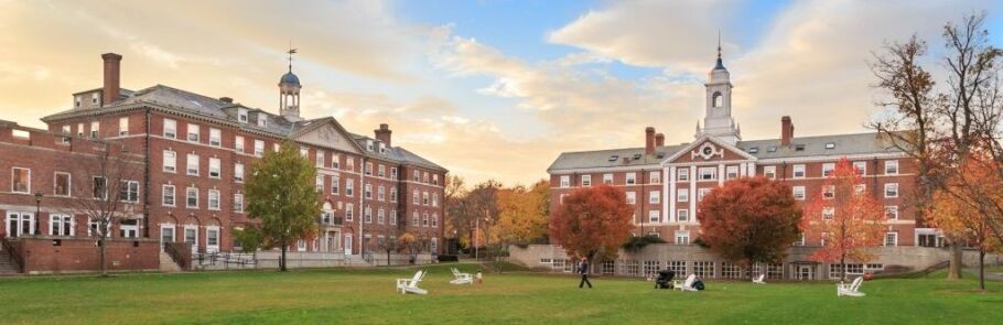 College campus buildings with autumn foliage and students on the lawn.