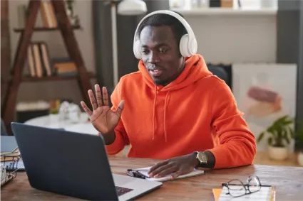 Student in orange hoodie video conferencing for college counseling session.